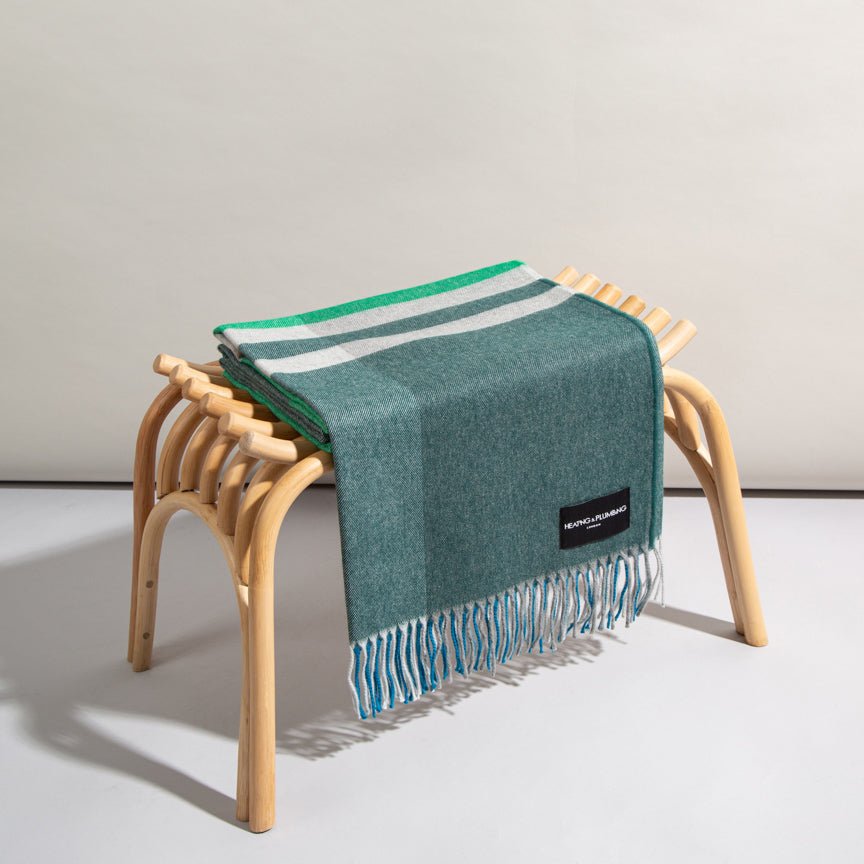 Green blanket with white stripes draped over a wooden stool on a light grey background