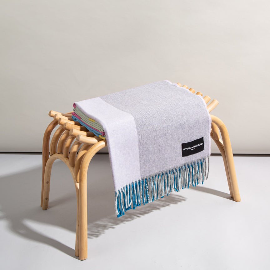 Blanket with blue fringe draped over a wooden stool on a light grey background