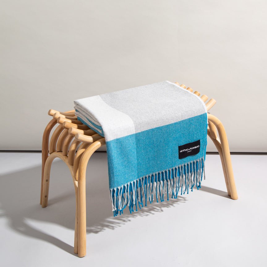 Blue and white striped throw blanket with fringes draped over a wooden stool on a light grey background