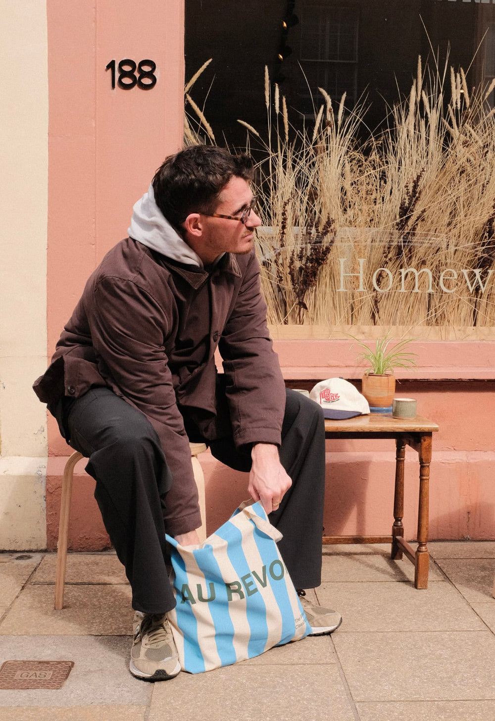 Man sitting outdoors with a blue and cream striped bag, pink building in the background