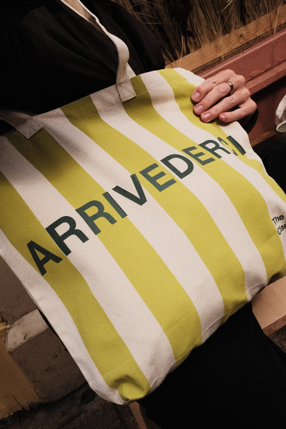 Person holding a yellow and white striped tote bag with 'ARRIVEDERI' branding.