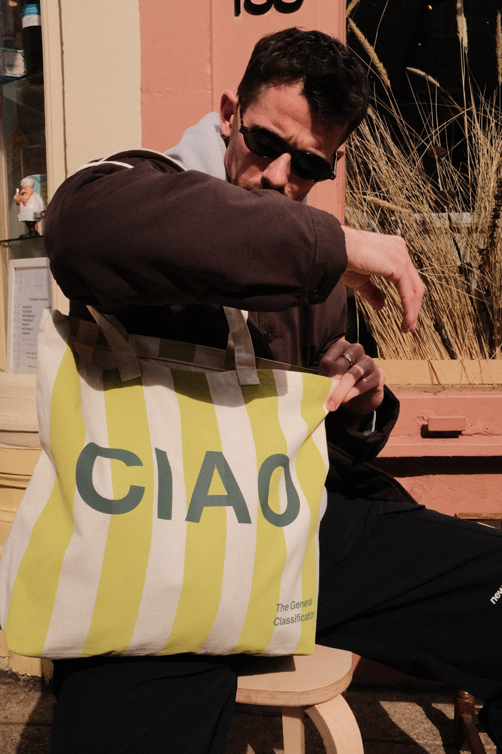 Person holding a yellow striped tote bag with 'CIAO' text outdoors.