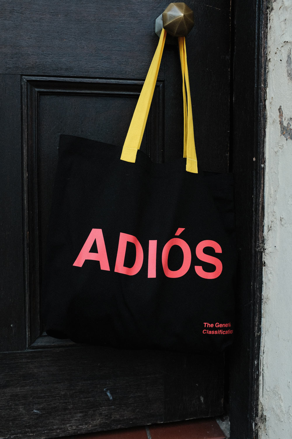 Black tote bag with 'ADIÓS' in red text on a black door.