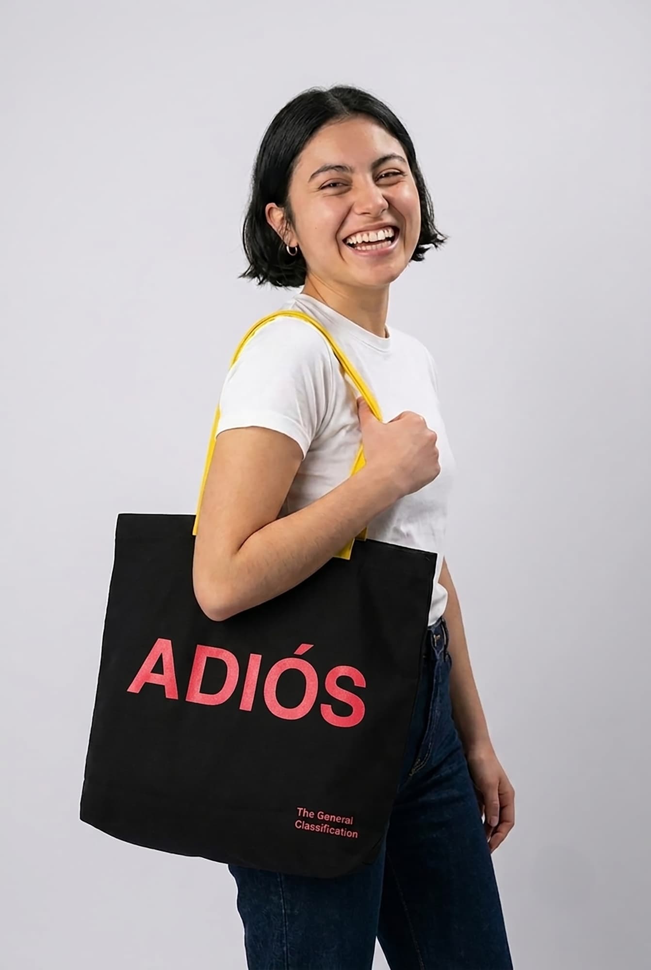 Person holding a black tote bag with 'ADIOS' in red text on a plain background