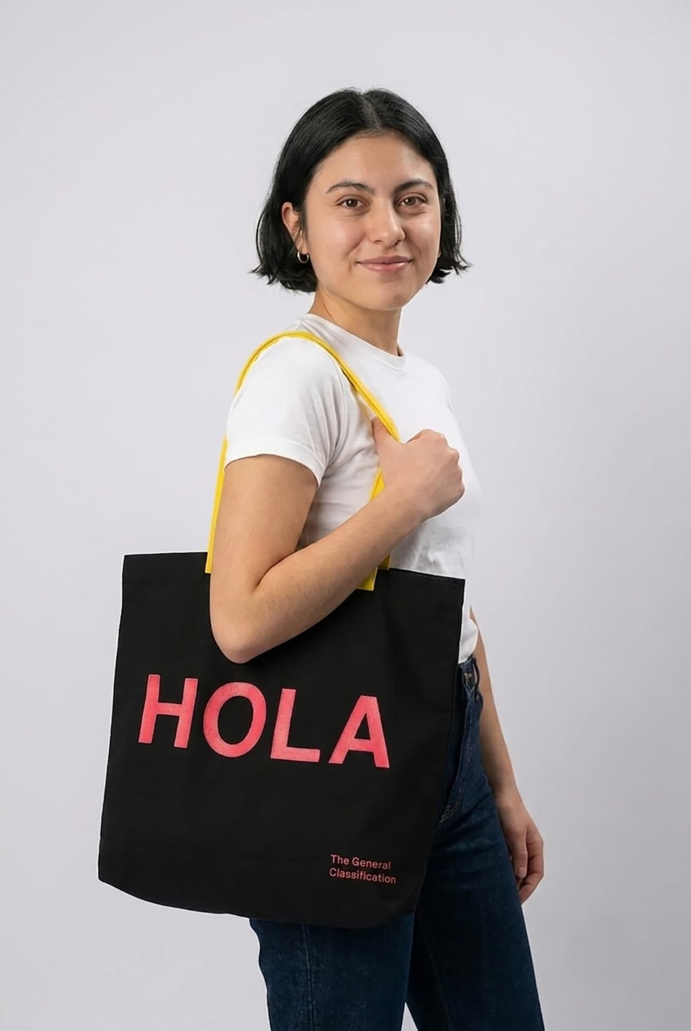Woman holding a black tote bag with 'HOLA' in pink text on a white background