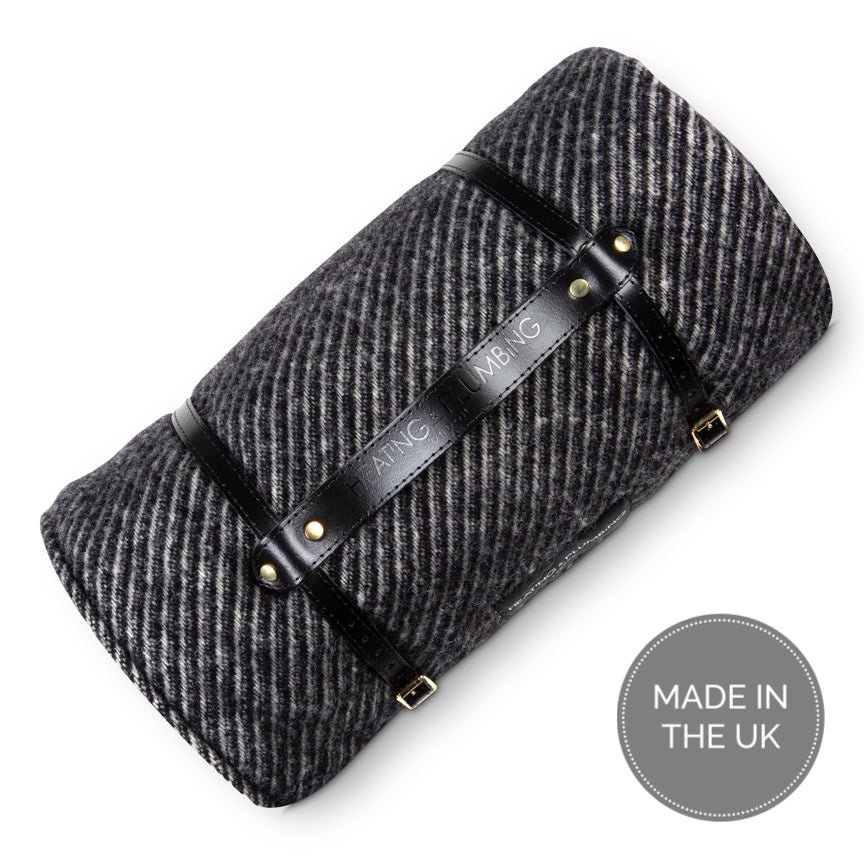 Grey herringbone blanket with black leather straps on a white background, featuring the brand 'Heating & plumbing'.