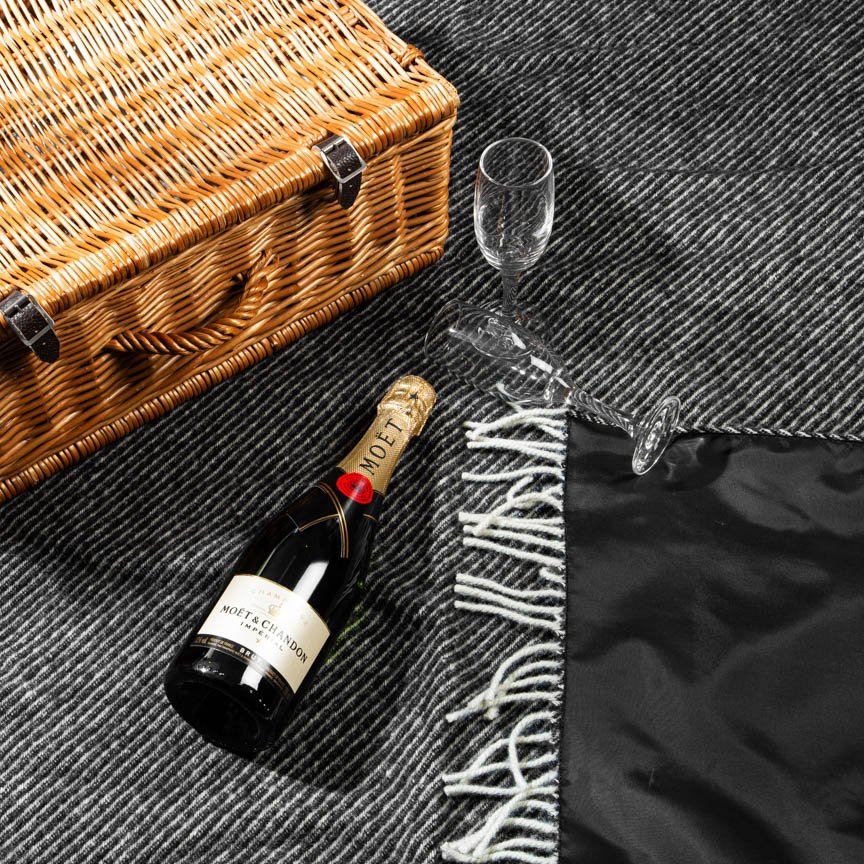 Bottle of champagne, wine glass, and picnic basket on a black herringbone blanket