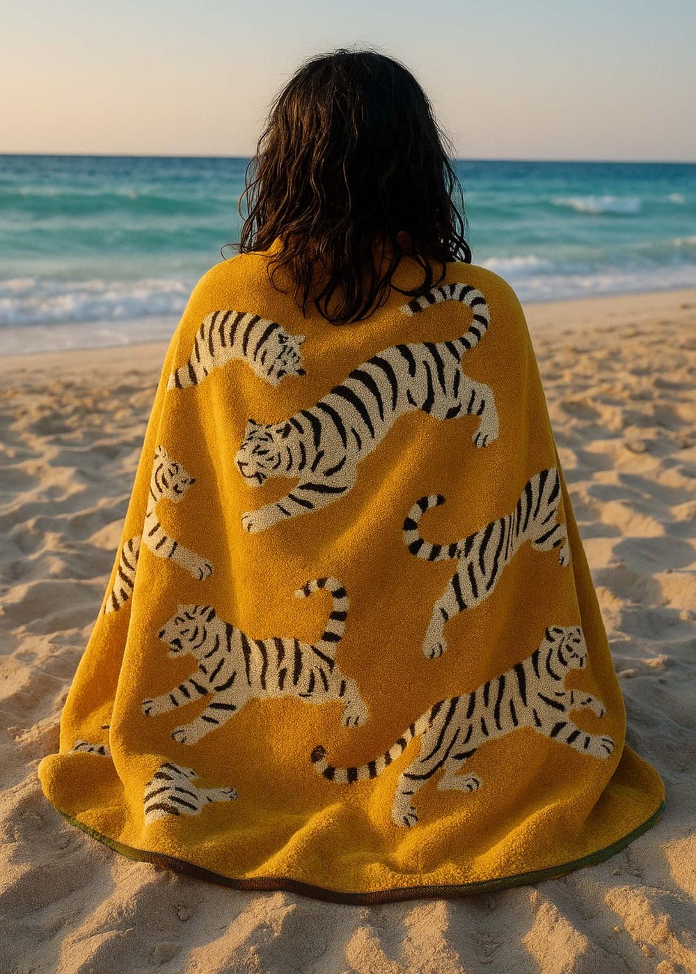 Person wrapped in a yellow towel with tiger patterns on a beach