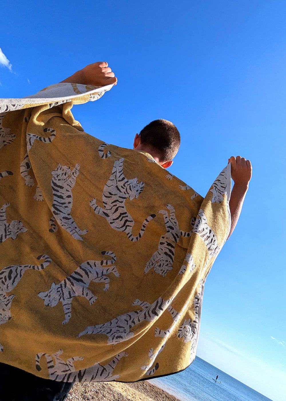 Person holding a yellow towel with tiger patterns against a clear blue sky.