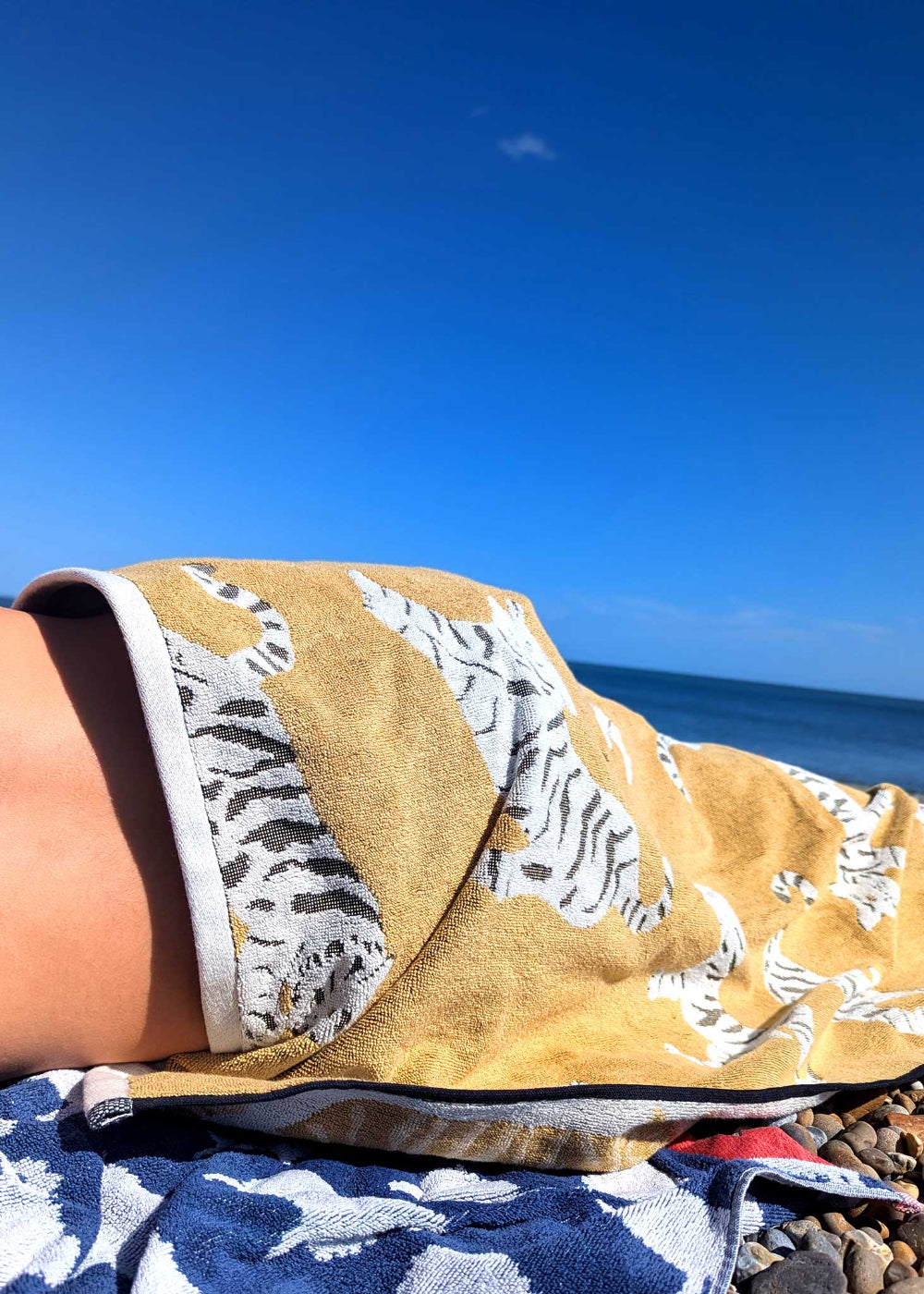 Person holding a yellow towel with a leopard pattern on a beach.
