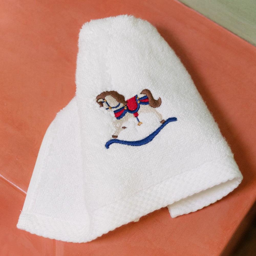 White towel with embroidered rocking horse christmas design on a red surface
