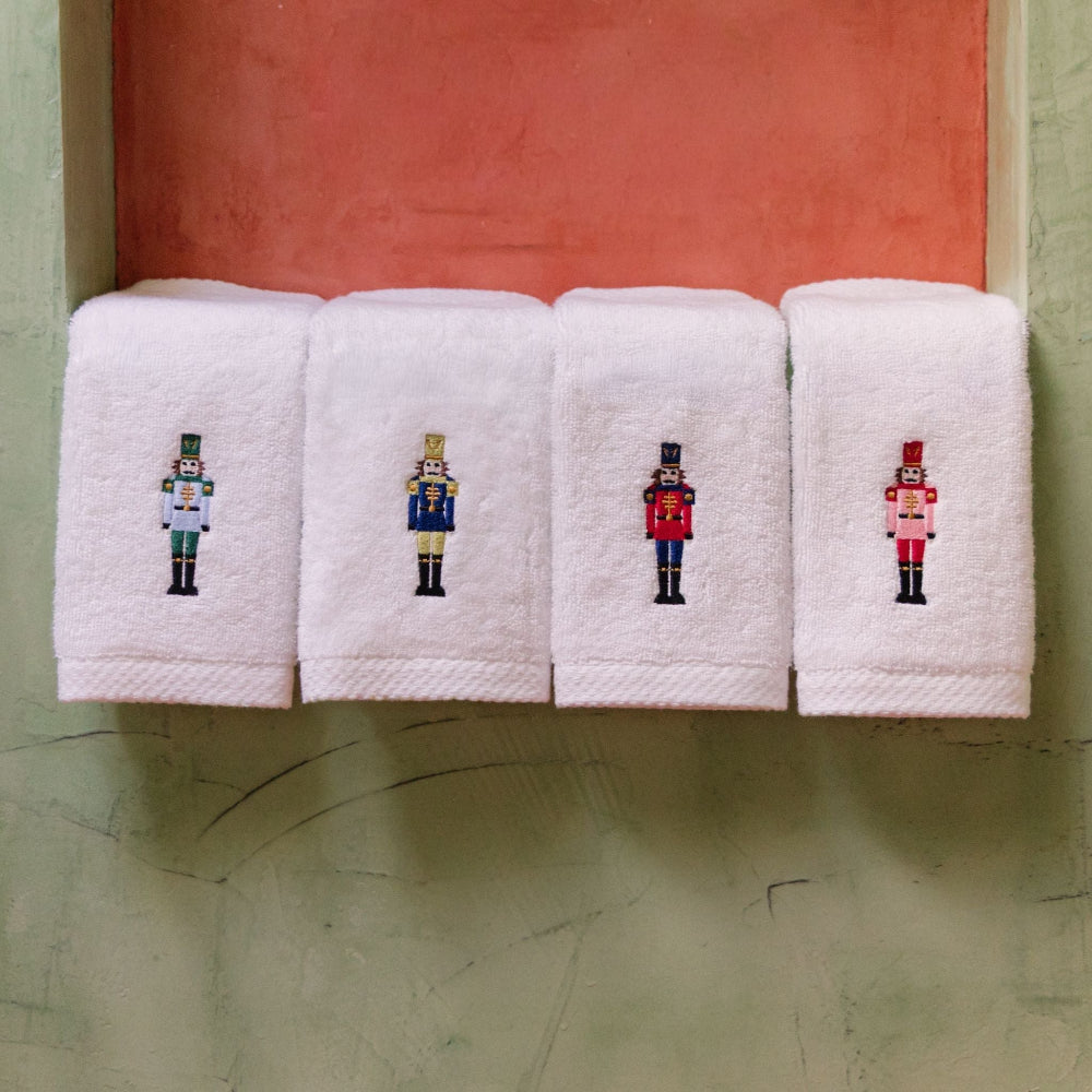 Four white towels with embroidered nutcracker designs on a textured surface.