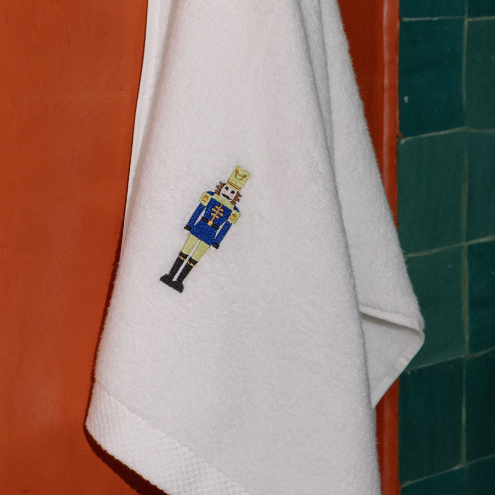 White towel with embroidered nutcracker design hanging on a red door.
