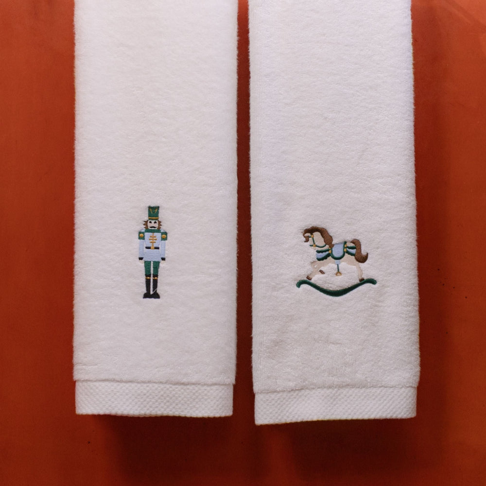 Two white towels with embroidered christmas designs on a red background