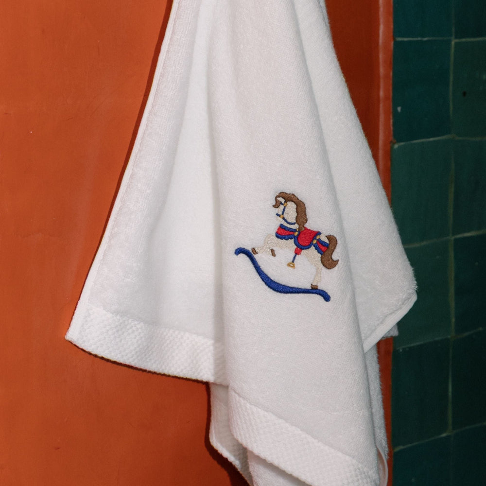 White towel with embroidered horse design hanging on a red wall.
