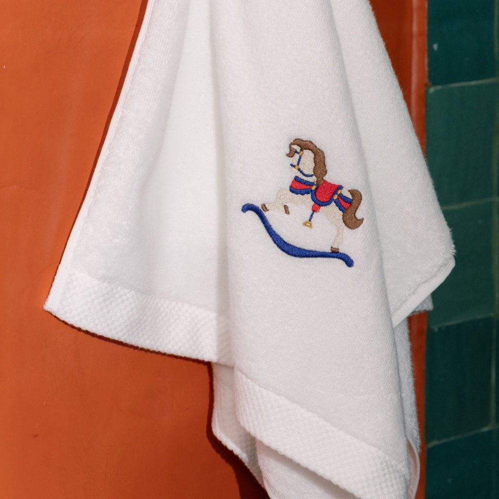 White towel with embroidered rocking horse design on a red and green tiled wall.
