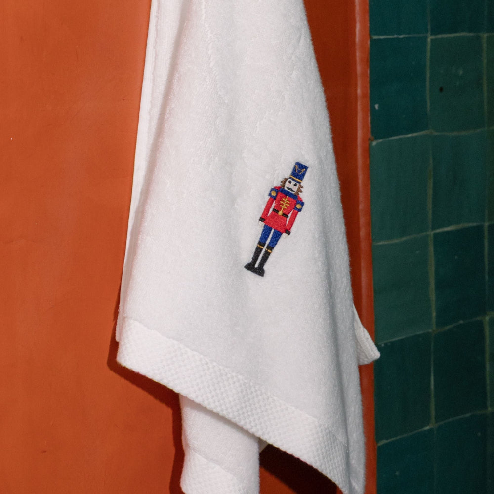 White towel with a embroidered nutcracker design hanging on a towel rack against a colourful wall.
