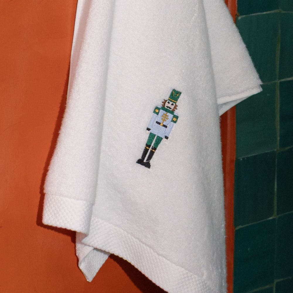 White towel with a embroidered nutcracker design hanging on a towel rack.