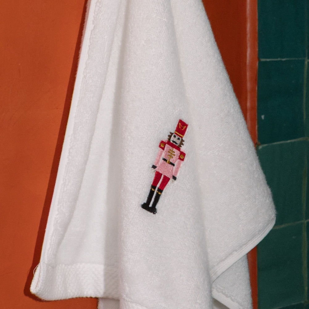 White towel with a embroidered nutcracker design hanging on a red door.