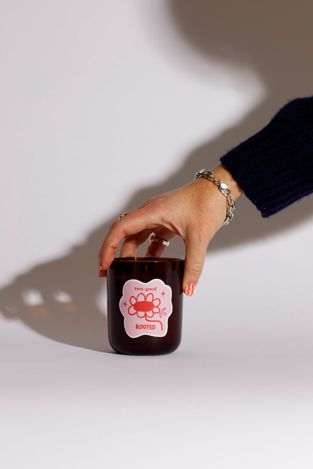 Hand holding a small brown candle jar with a red label called rooted against a white background