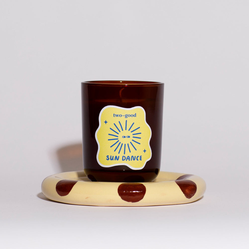 Brown candle with a label on a polka dot stand against a light grey background