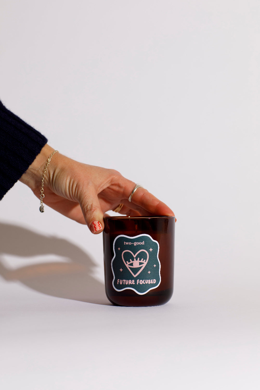 Hand holding a brown candle with a label two good on a white background