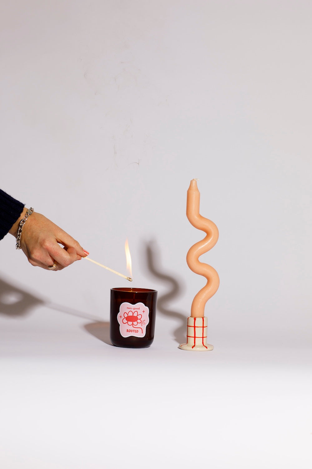 Person lighting a candle with a wavy candle next to it on a plain background