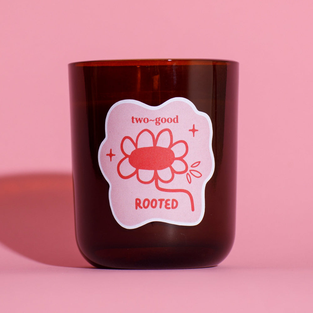 Brown candle with a pink label featuring a flower design on a pink background