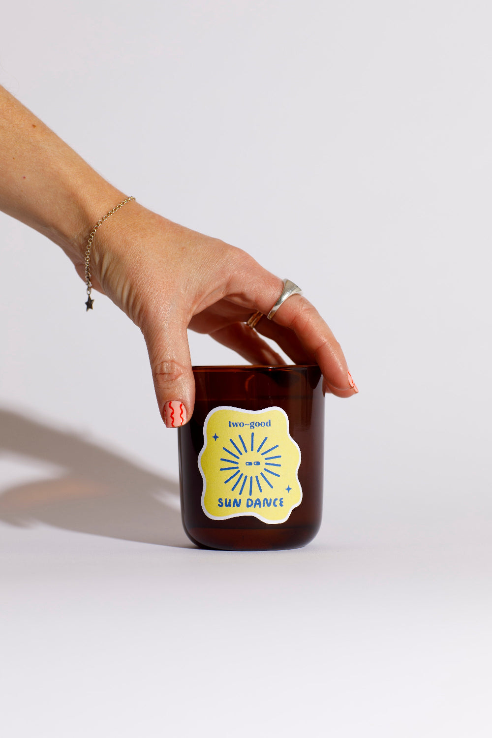 Hand holding a brown candle with a yellow label against a white background