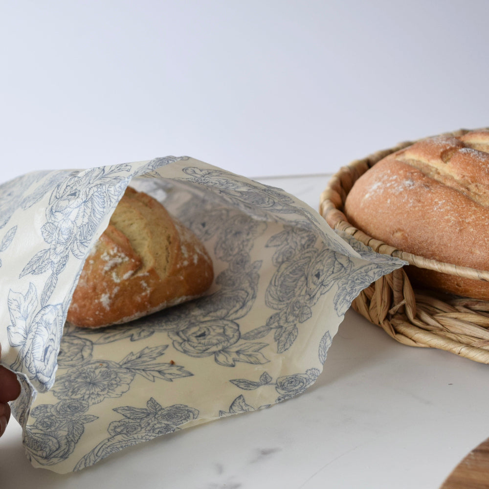 Loaf of bread wrapped in a floral-patterned beeswax bag on a marble surface.