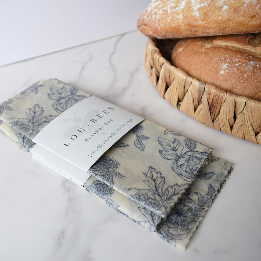 Folded beeswax bag with floral pattern and 'Lou-Bee's' packaging on a marble surface with bread in the background