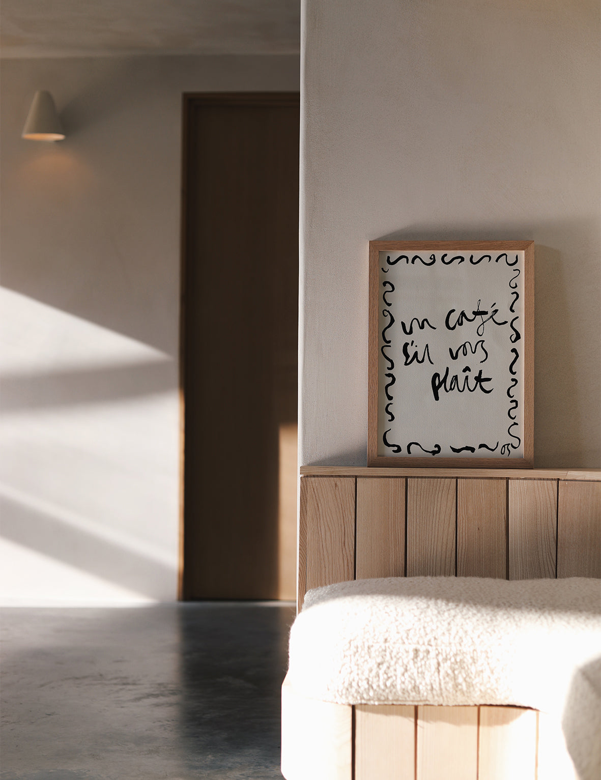 Modern interior with a framed quote 'un cafe sil vous plait' on a wall above a wooden headboard.