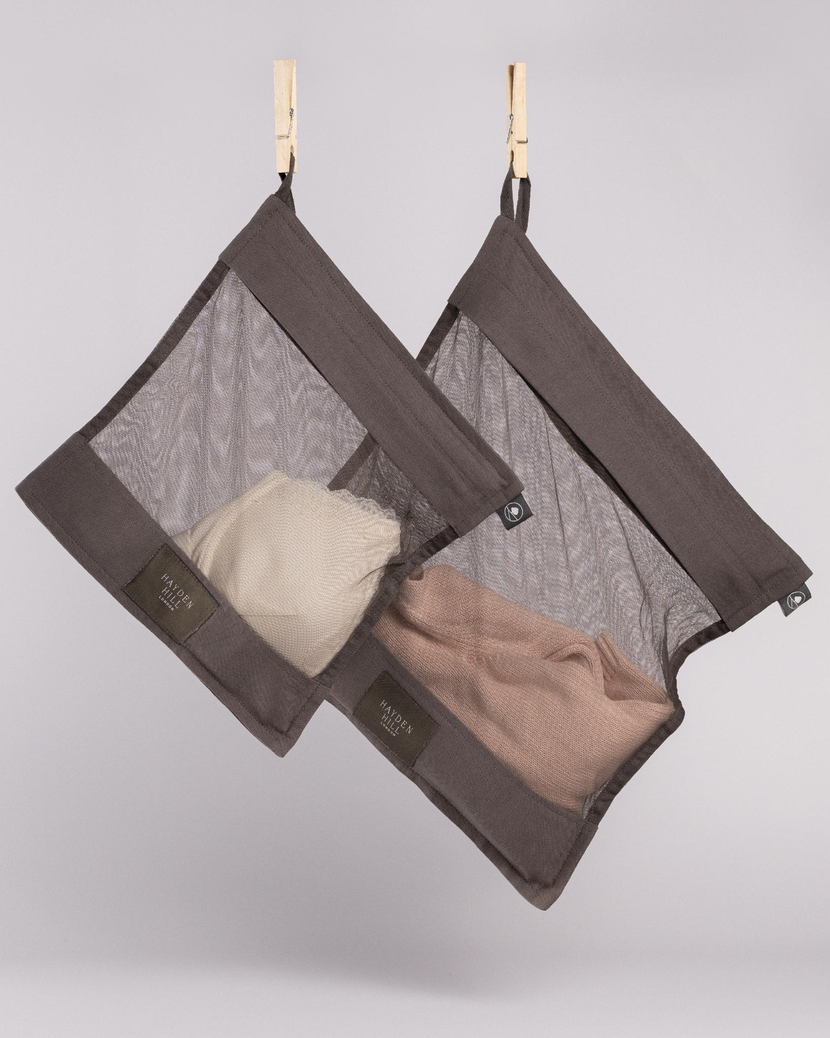 Two brown mesh laundry bags with clothes inside, hanging on a gray background