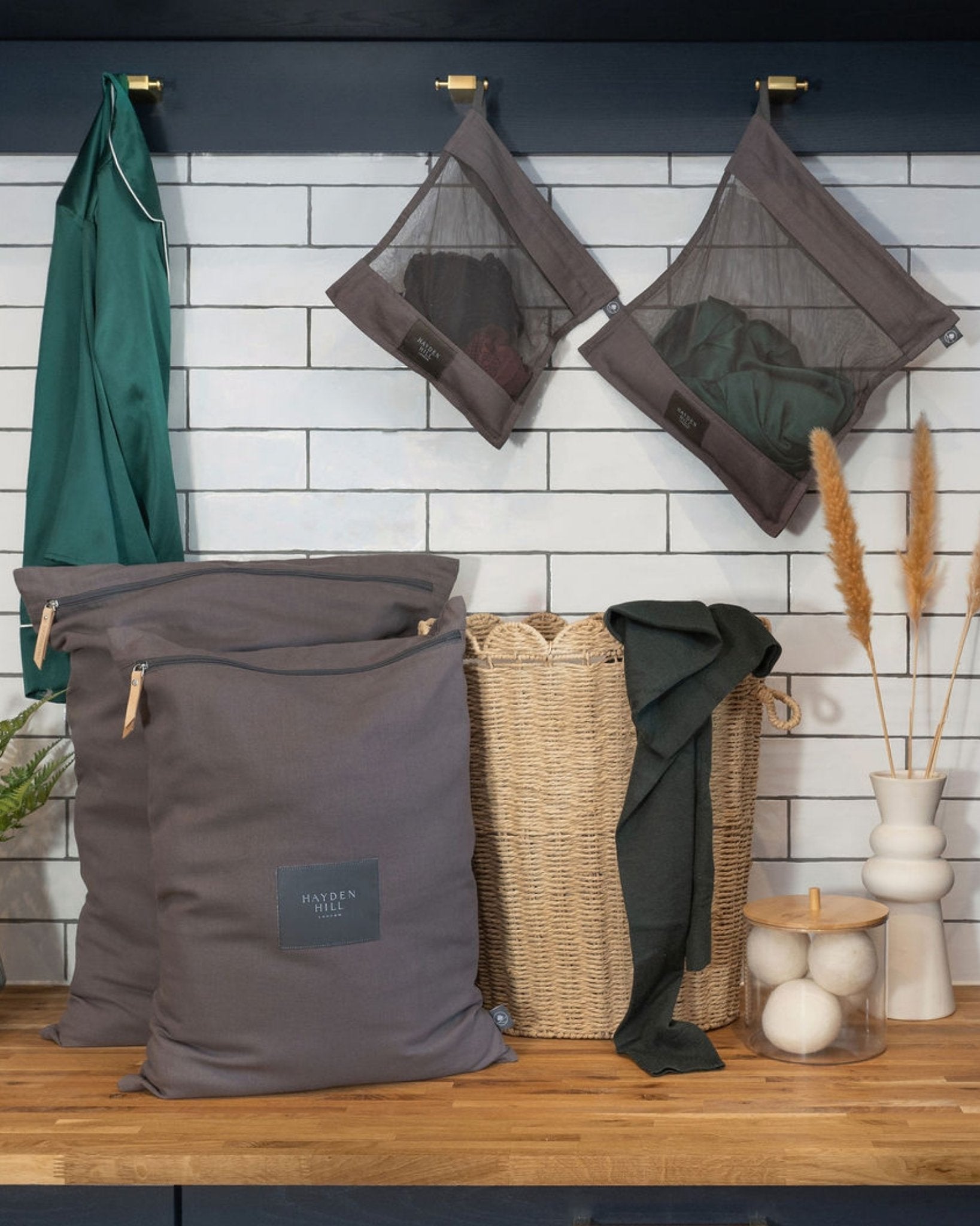 Gray laundry bags with a woven basket on a wooden surface against a tiled wall.