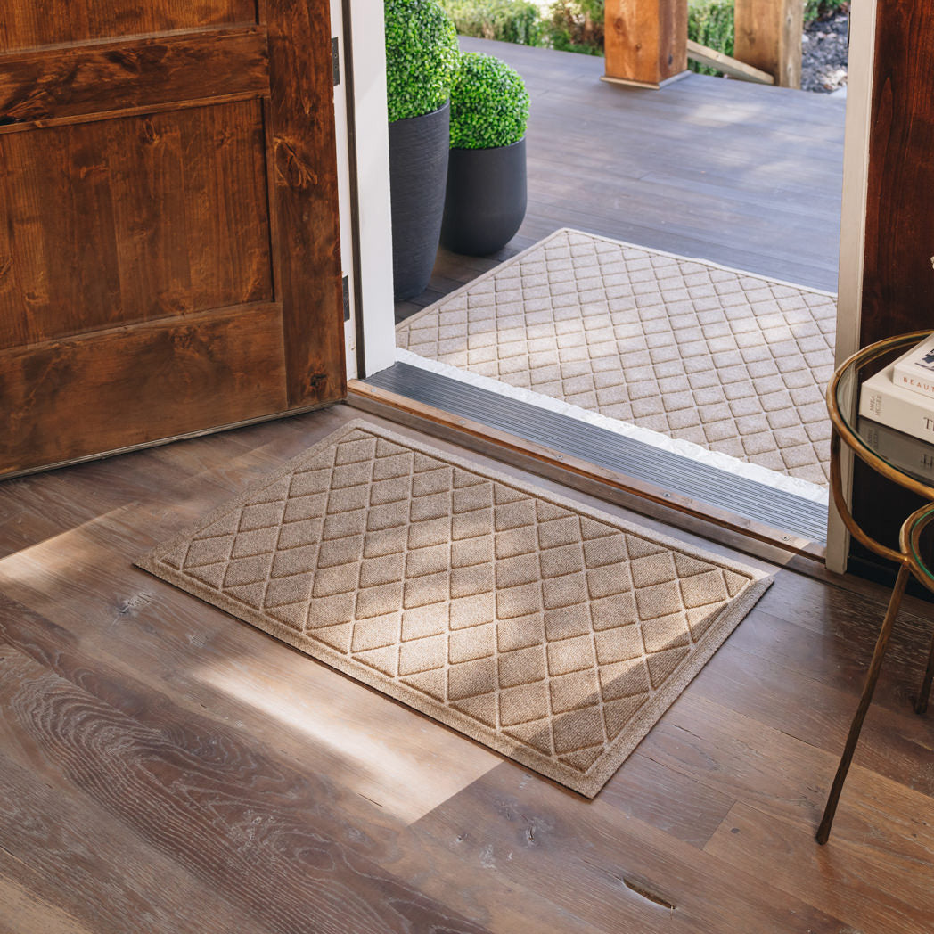 Camel WaterHog Argyle doormats placed on both sides of an open wooden entrance door.