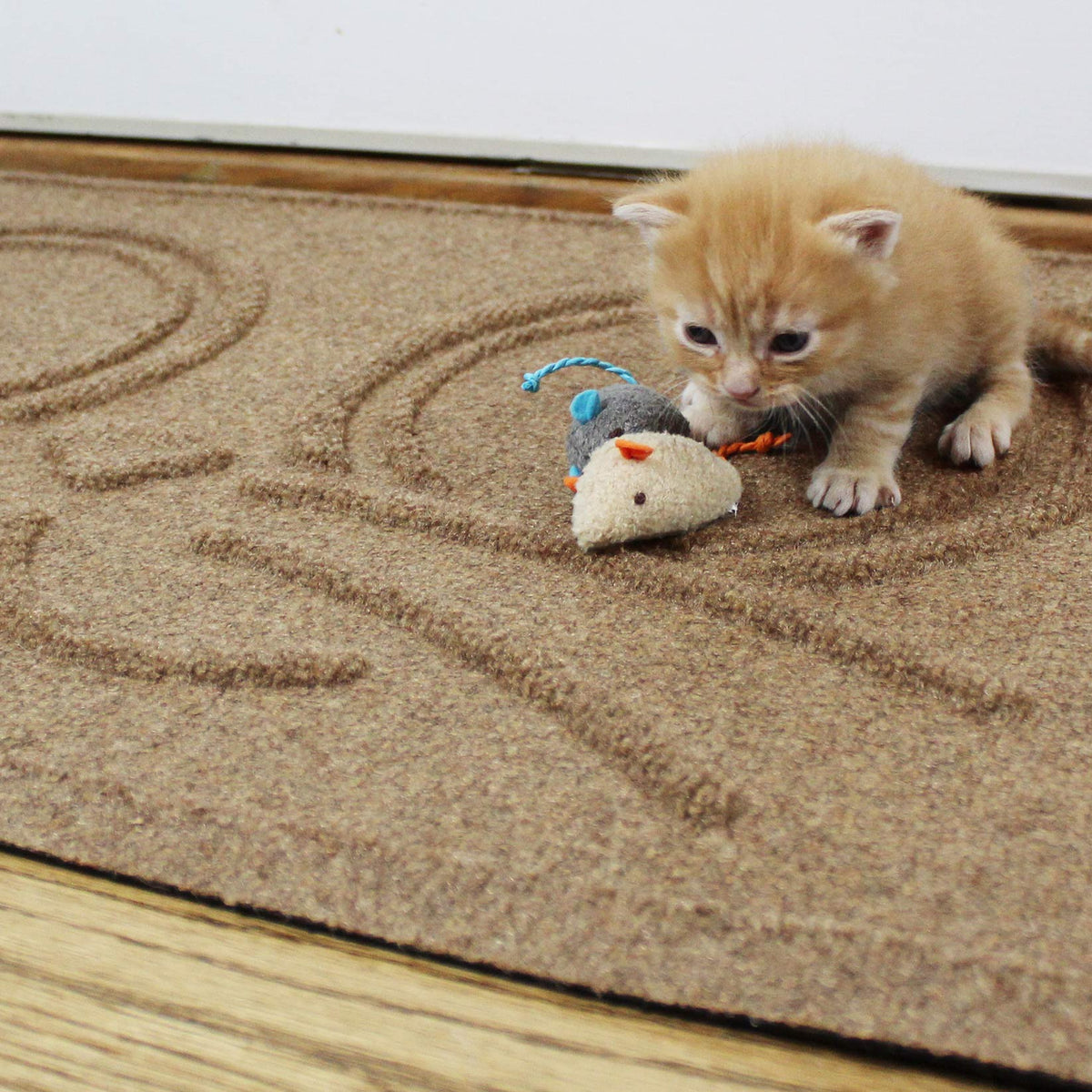 Ginger kitten playing with a soft toy on a Camel WaterHog Kitty Face Mat, showing the raised whisker pattern.