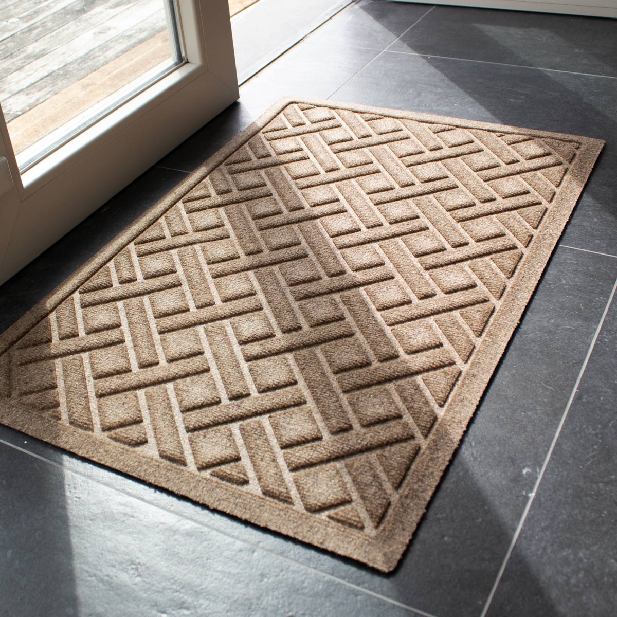 Camel WaterHog Lattice doormat on a grey tiled floor beside a glass door leading to a wooden deck.