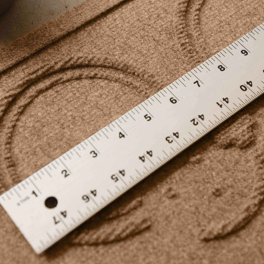 Close-up of a measuring ruler placed across the raised circular feeding area of a Camel WaterHog Puppy Face Mat.