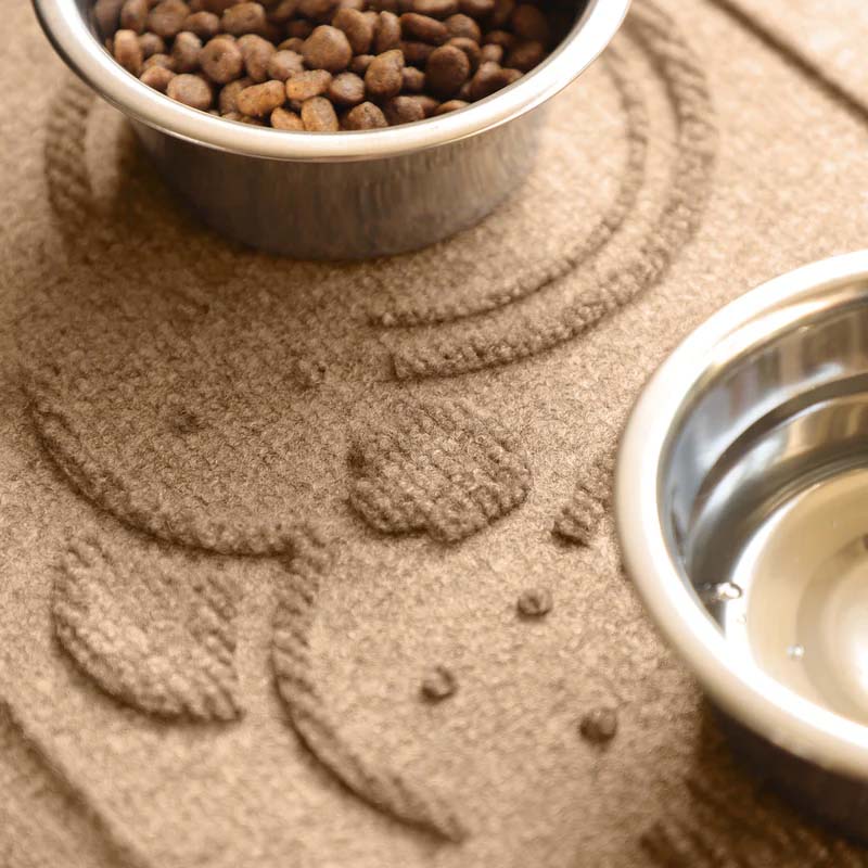 Close-up of the raised puppy nose and mouth pattern on a Camel WaterHog feeding mat between two stainless steel pet bowls.