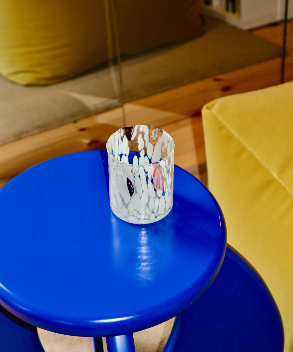 Blue stool with white bright colourful murano glass on top in a room setting.
