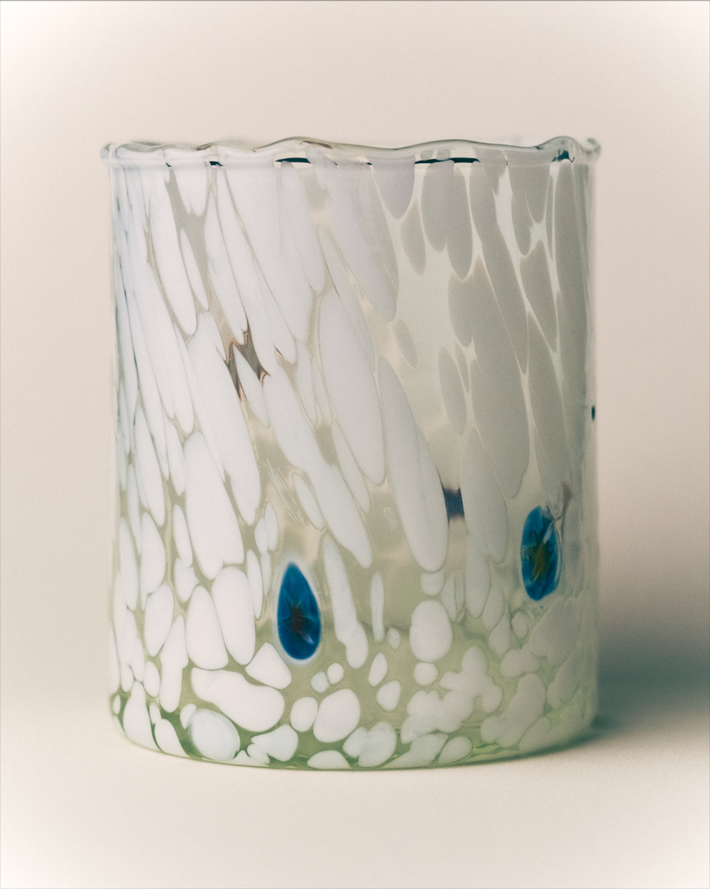 Decorative glass tumbler with white patterns and blue accents on a beige background