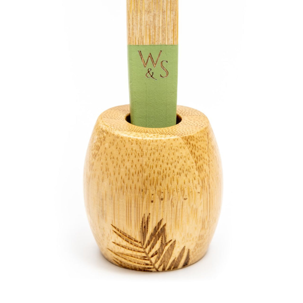 Bamboo toothbrush holder with a green tipped toothbrush inside on a white background