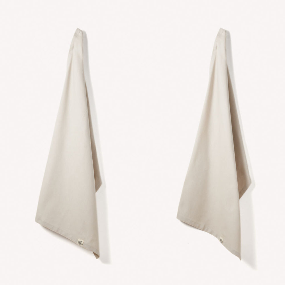 Two beige towels hanging on a white background