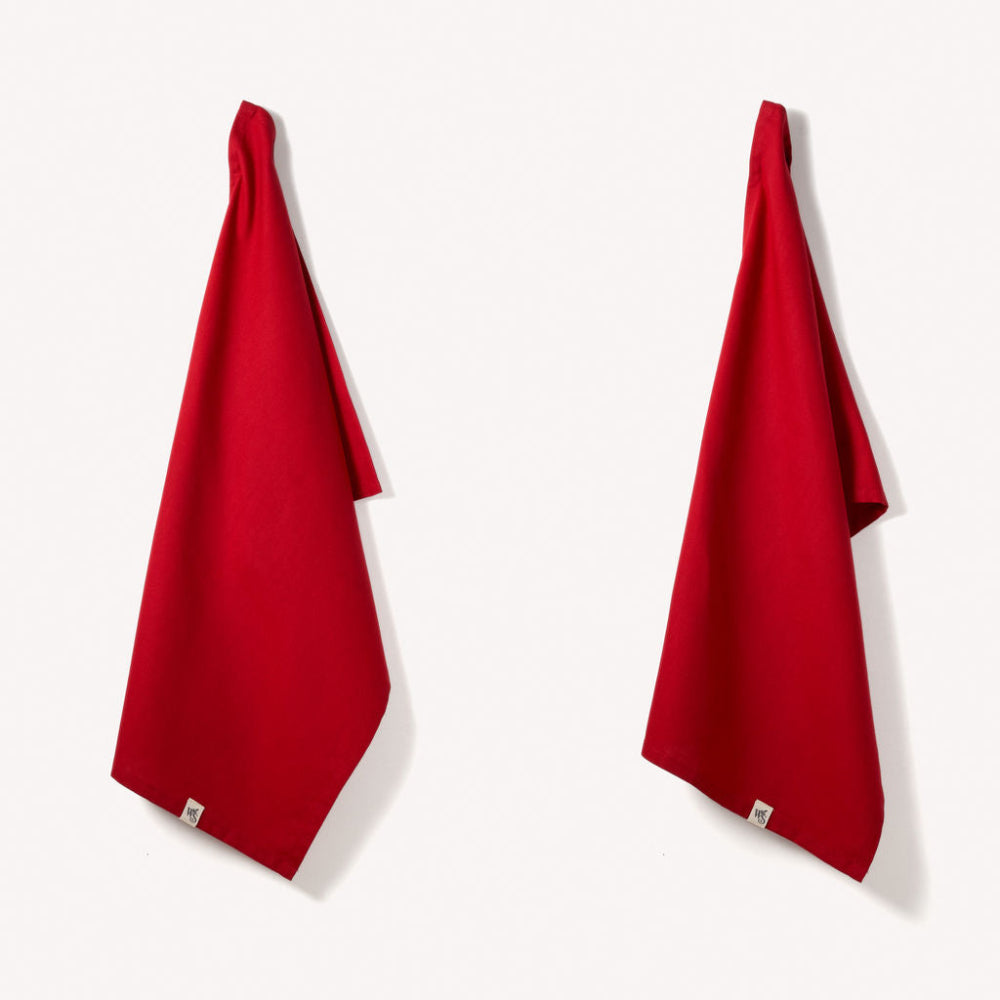 Two red organic tea towels hanging on a white background