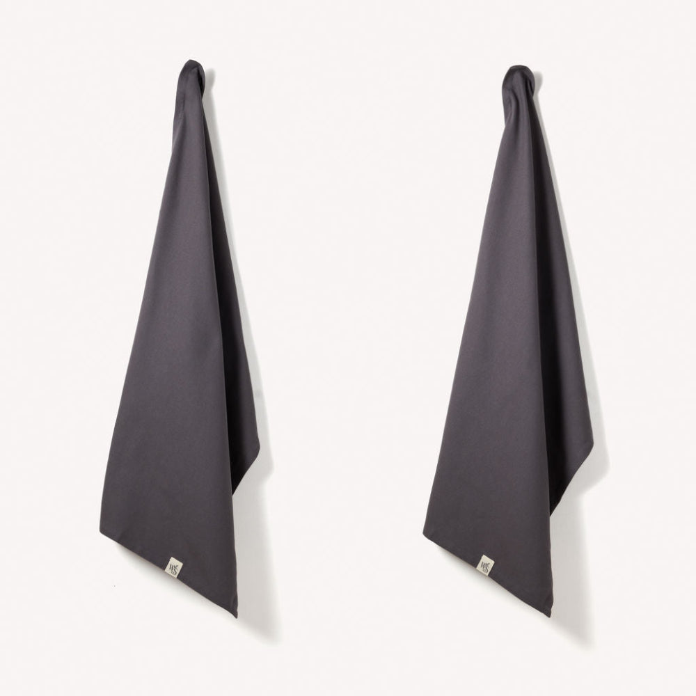 Two dark grey herringbone organic tea towels hanging on a white background