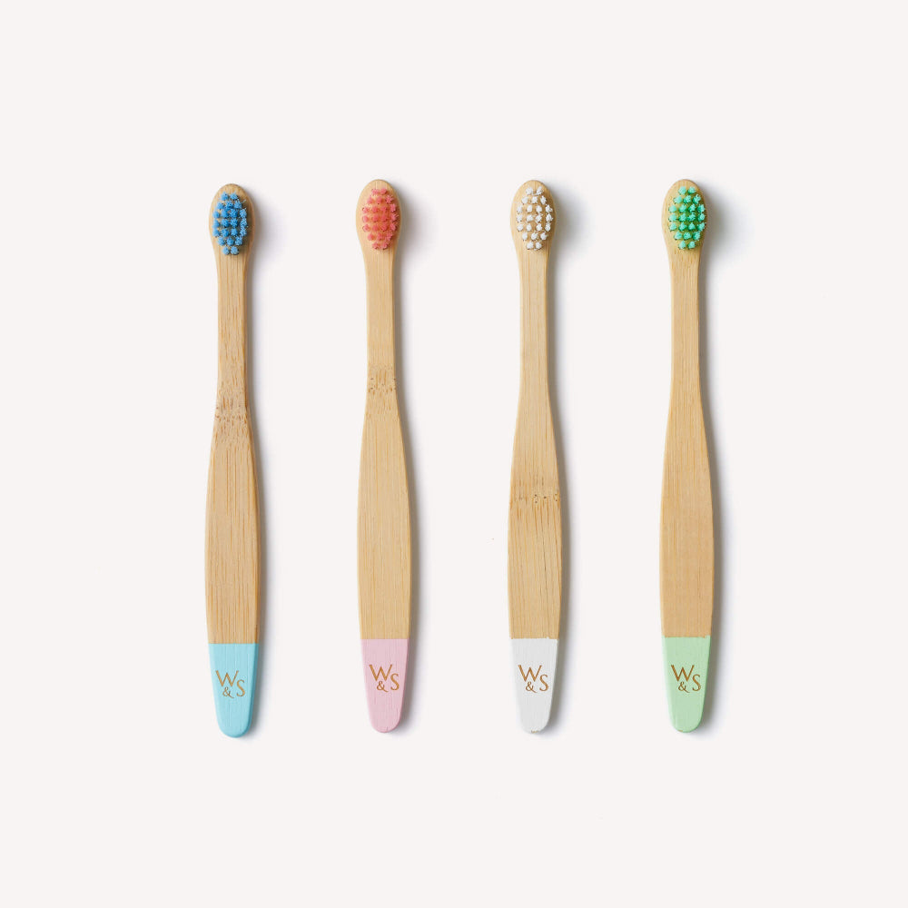 Four bamboo toothbrushes with coloured bristle heads and pastel handles on a white background.