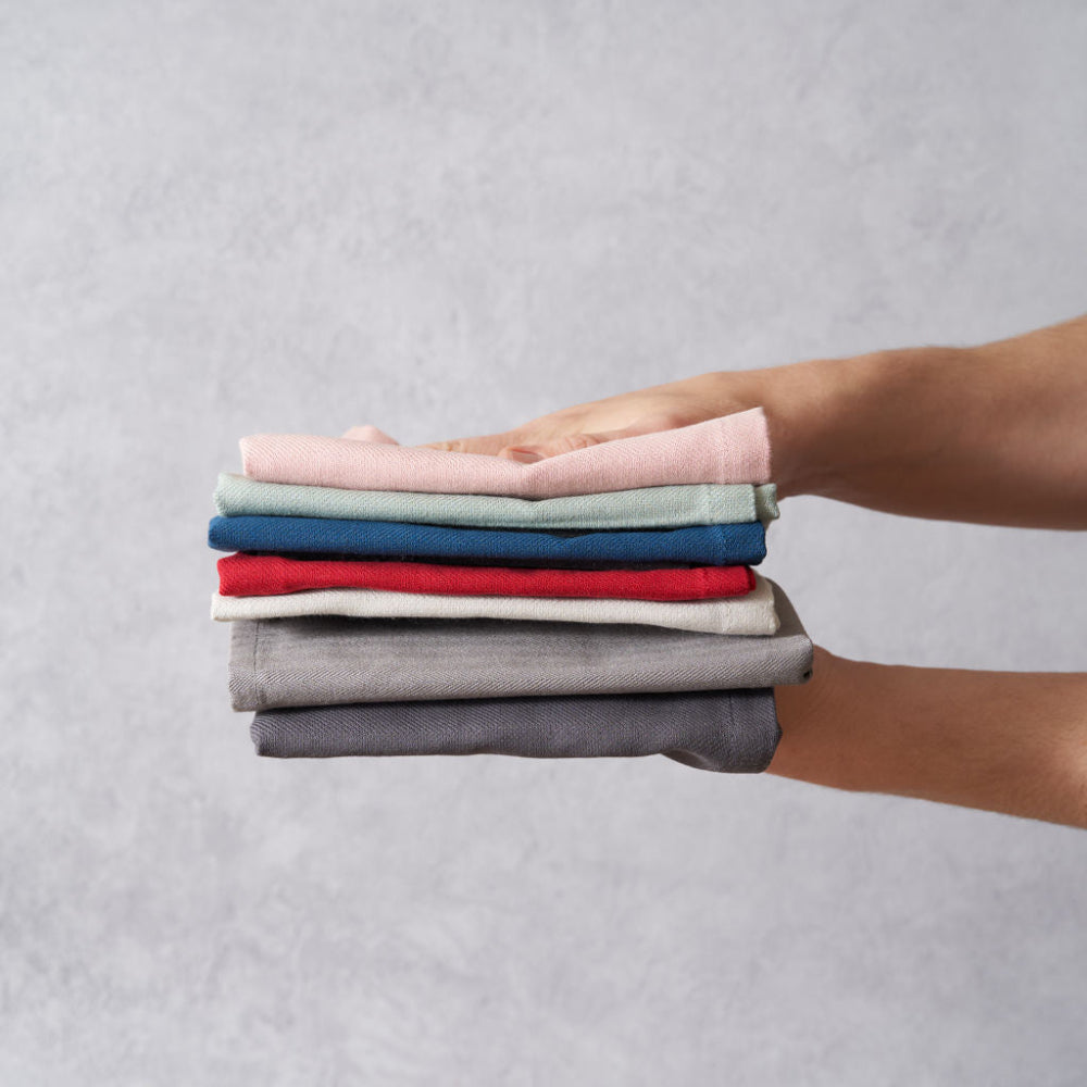 Stack of folded multi coloured organic tea towels held by a person against a grey background