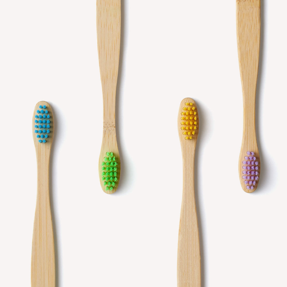 Set of four bamboo toothbrushes for kids with coloured bristles on a white background