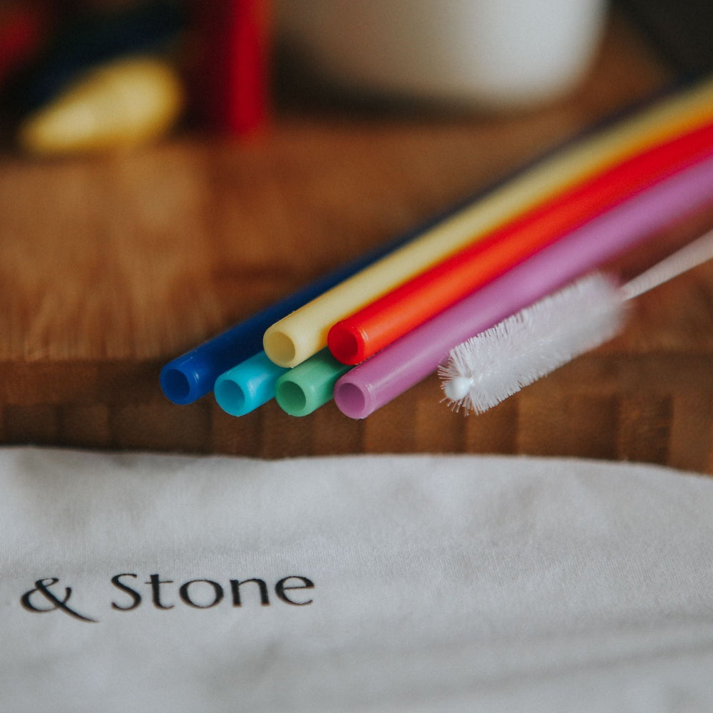 Colourful silicone straws with a cleaning brush on a wooden surface, featuring the brand 'Wild & Stone'.