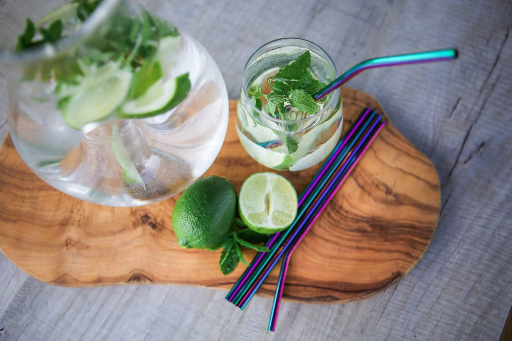 Glass of water with lime and mint on a wooden board with colourful stainless steel straws.
